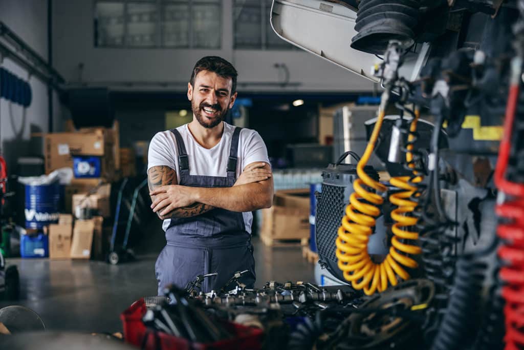 Smiling happy bearded tattooed worker in overalls standing next